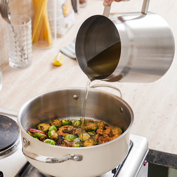 Stirring vegetables in a pot on a stove with a ladle pouring liquid.